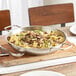 A Vigor SS1 Series stainless steel fry pan filled with pasta, mushrooms, and herbs on a wooden board.