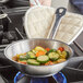 A Vigor stainless steel fry pan on a stove with vegetables in it.
