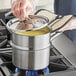 A person using a Vigor stainless steel double boiler on a stove.