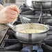 A hand using a whisk to stir food in a Vigor stainless steel saucier pan.