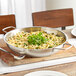 A Vigor stainless steel fry pan filled with pasta and greens on a wooden table.