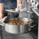A person using a Vigor stainless steel brazier to cook soup with meat and vegetables.