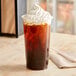 A EcoChoice PLA compostable plastic cup filled with a drink and whipped cream on a counter.