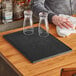 A black Choice bar mat on a wood counter with a pair of glasses on it.