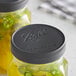A Ball wide mouth canning jar filled with green liquid and jalapeno peppers with a black plastic lid.