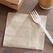 A plastic fork on a 12" x 12" natural kraft 1/4 fold luncheon napkin.
