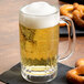 A Libbey beer mug filled with beer on a table with pretzels.