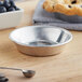 A Baker's Mark mini aluminum pie pan filled with blueberries on a table with a spoon.