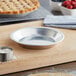 A Baker's Mark aluminum pie pan on a wooden cutting board with a bowl of flour.