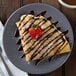 A plate of crepes with chocolate syrup and strawberries on a table.