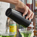 A bartender using an Arcoroc Matte Black Stainless Steel Bar Shaker Tin to pour a green drink into a martini glass.