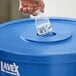 A hand putting a plastic bottle into a blue Lavex recycling container with a round lid with a 3 1/2" hole.