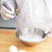 A person in a white coat using a Vollrath stainless steel whisk to mix eggs in a bowl.