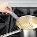 A hand holding a Vollrath Jacob's Pride stainless steel whisk over a pot of food.