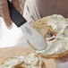 A person using a Mercer Culinary black scalloped sandwich spreader to spread cream cheese on a bagel.