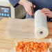 A person cutting a roll of Choice Full Mesh External Vacuum Packaging Bags with a knife on a table.