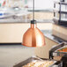 A ServIt modern copper ceiling mount heat lamp over food on a table.