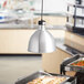A table with food in a stainless steel tray and a container underneath a ServIt ceiling mount heat lamp.