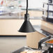 A ServIt black ceiling mount heat lamp with a retractable cord hanging over a buffet table.