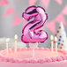 A pink birthday cake with a pink balloon shaped like the number two on top.