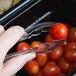 A person using Cambro clear plastic tongs to serve a tomato at a salad bar.