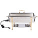 A Vollrath stainless steel electric chafing dish on a table with a plug on the side.
