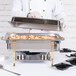 A chef preparing food in a Vollrath Classic Brass Trim electric chafing dish on a table.