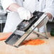 A person using a Bron Coucke stainless steel professional vegetable slicer to cut carrots on a table.