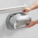 A hand opening a silver San Jamar double roll toilet paper dispenser.