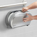 A hand opening a silver San Jamar double roll toilet paper dispenser.