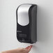 A person using a black and silver San Jamar hand soap dispenser on a wall.