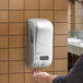 A person using a San Jamar Summit Rely Silver hybrid automatic hand soap, sanitizer, and lotion dispenser.