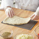 A person's hand rolling American Metalcraft Hard Coat Anodized Aluminum flatbread dough on a pizza screen.