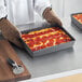 A person holding a Detroit-style pizza in an American Metalcraft hard coat anodized aluminum pan.