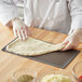 A person using an American Metalcraft Hard Coat Anodized Aluminum Mega Flatbread Screen to make pizza dough on a table.