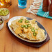 An oval aluminum sizzler platter with nachos, cheese, and jalapenos.
