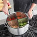 A person using a Choice vegetable and pasta cooker set to cook vegetables in a large pot.