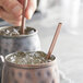 A person holding an Acopa copper stainless steel straw in a metal cup with ice.