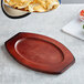 A wooden oval underliner with mahogany finish holding a plate of tortilla chips with cheese.