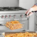 A person using a 9 1/2" x 7 1/4" Fryer Basket to fry french fries.