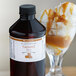 A bottle of LorAnn Oils Caramel flavoring liquid next to a glass of ice cream.