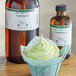 A cupcake in a paper wrapper with lemongrass frosting next to a bottle of LorAnn Oils Lemongrass flavor.