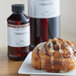 A cinnamon roll on a plate next to a bottle of LorAnn Oils Cinnamon Roll flavoring.