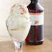 A glass with a scoop of ice cream and a bottle of LorAnn Peach Super Strength Flavor syrup.