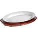 A white oval aluminum sizzler platter with mahogany finish rubberwood underliner on a wooden stand.