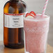 A glass of pink strawberry banana drink next to a brown LorAnn Oils bottle.
