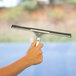 A hand using a Carlisle window squeegee with a steel handle.