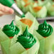 A hand using Rich's Green Buttrcreme icing to frost a cupcake.