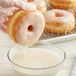 A hand dipping a Rich's glazed doughnut into a bowl of milk.