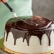 A person using a knife to cut a chocolate cake with Rich's Dark Chocolate Ganache Icing.